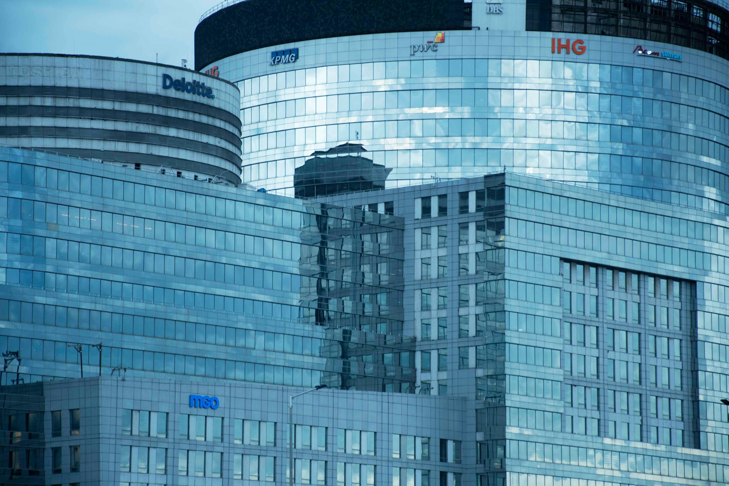 Glass skyscrapers reflecting the sky, showcasing brand logos under a calm sky.